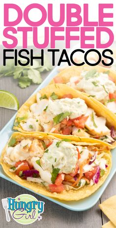 two fish tacos on a blue plate with limes and cilantro in the background