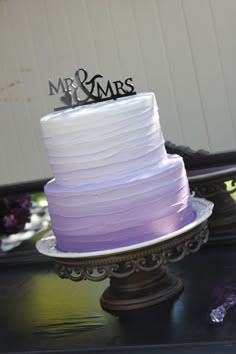 a purple and white cake sitting on top of a metal stand next to a mirror