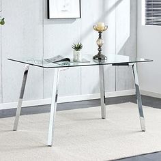 a glass table with metal legs in front of a white wall and carpeted floor