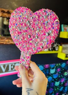 a person holding up a pink heart shaped object with lots of small beads on it