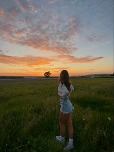 a woman standing in a field at sunset with her arms around her back, looking up into the sky