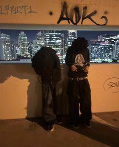 two people standing next to each other in front of a wall with graffiti on it