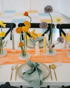 the table is set with yellow and orange flowers in vases, candles, and napkins