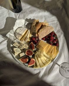 an assortment of cheeses, fruit and wine on a plate with a glass of wine