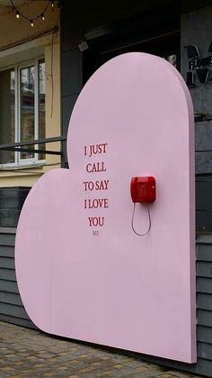 a pink heart shaped sign with words written on the front and side, sitting in front of a building