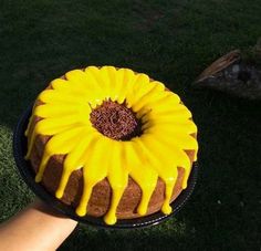 a cake with yellow icing sitting on top of a black plate in the grass