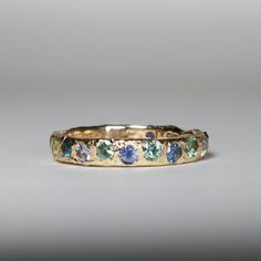 a yellow gold band with blue and green stones on the inside, set against a gray background