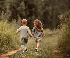 two young children walking down a dirt path in the middle of tall grass and trees