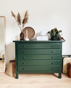 a green dresser sitting in front of a mirror next to a basket and plant on top of it