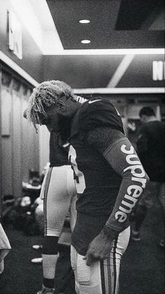 a black and white photo of a football player in the locker room with his head down