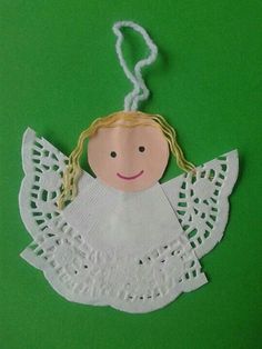 a paper angel ornament hanging on a green background with twine and thread