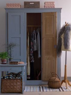 an open closet with clothes hanging on the door and a basket in front of it