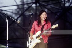 a woman playing guitar and singing into a microphone on stage at an outdoor music festival