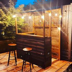 an outdoor bar with stools and lights on the outside wall, next to a wooden deck