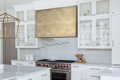 a kitchen with white cabinets and marble counter tops, an oven hood over the stove