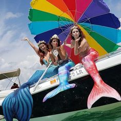 three mermaids sitting on the back of a boat under an umbrella