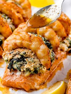 a spoon is being drizzled with sauce on top of baked shrimp and spinach