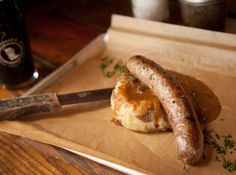 two sausages on top of a piece of paper next to a knife and beer