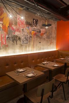 an empty restaurant with wooden tables and brown leather booths, graffiti on the wall behind them