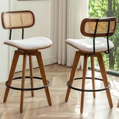 two wooden barstools with white upholstered cushions sit in front of a window