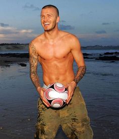 a shirtless man holding a soccer ball in his hands on the beach at sunset