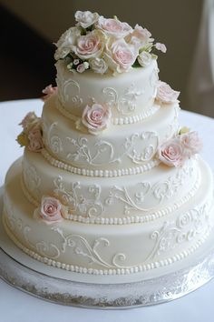 Elegant four-tier white wedding cake adorned with delicate pink roses and intricate icing designs. 1960s Wedding Cake, French Country Wedding Cake, White And Peach Wedding Cake, Wedding Cake With Frosting Flowers, Vintage Wedding Cakes Elegant, Cute Simple Cake Designs, Vintage Style Wedding Cake, Wedding Cakes Pink, Trendy Wedding Cake