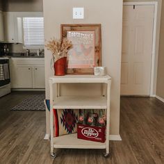 a shelf with some soda cans on top of it in a living room next to a kitchen