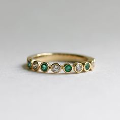 a yellow gold ring with green and white stones on the side, sitting on a plain surface