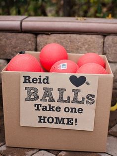 a cardboard box filled with red balls sitting on top of a brick floor next to a wall