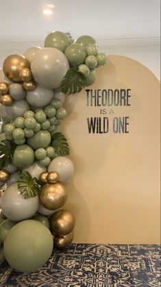 the balloon arch is decorated with gold and silver balloons, palm leaves, and greenery