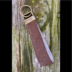 a brown leather keychain hanging from a tree trunk with moss growing on it