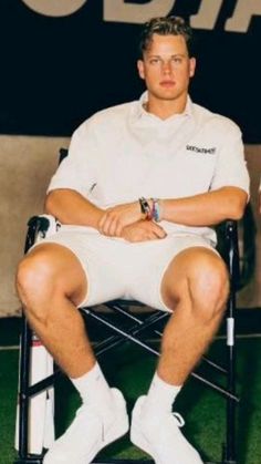 a man sitting in a chair holding a tennis racquet on top of a field