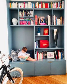 a boy is reading on the floor in front of bookshelves and a bicycle