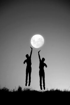 two people jumping up into the air with their arms raised in front of a full moon