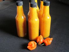 three bottles filled with yellow sauce and some orange peppers