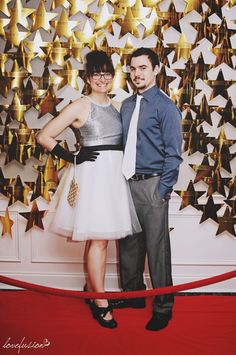 a man and woman standing next to each other in front of a wall with gold stars