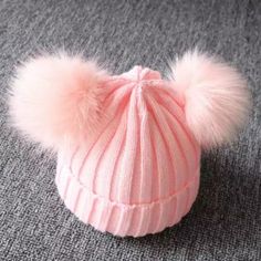 a pink hat with two pom poms on the top, sitting on a gray carpet