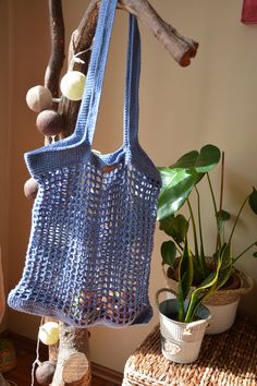 a blue crocheted bag hanging from a tree branch next to a potted plant