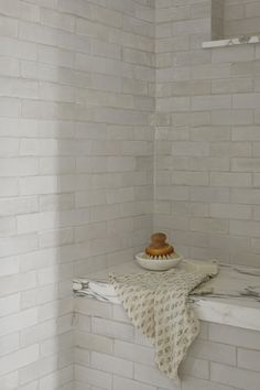 a white tiled shower with a bowl on the counter