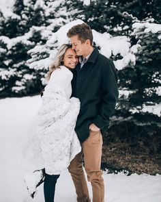 a man and woman are standing in the snow with their arms wrapped around each other