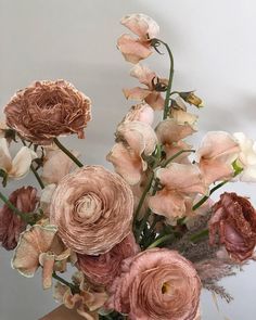 a vase filled with lots of pink flowers on top of a wooden table next to a white wall