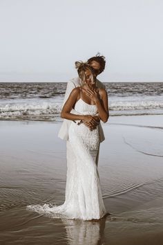 a woman in a white dress standing on top of a beach next to the ocean