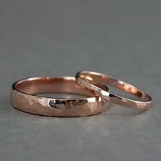 two gold wedding rings sitting next to each other on top of a gray surface,