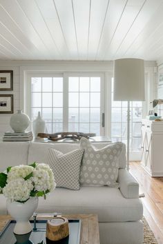 a living room filled with white furniture and flowers on top of a wooden coffee table