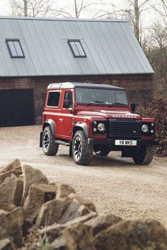 a red land rover parked in front of a barn