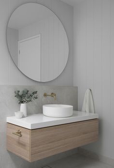 a white sink sitting under a round mirror next to a wooden cabinet and counter top