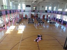 an indoor basketball court is decorated with pink and white balloons, streamers, and chairs