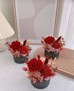 two vases filled with red flowers on top of a table next to a mirror