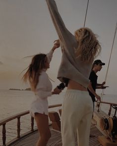 two people standing on the deck of a boat with their arms up in the air