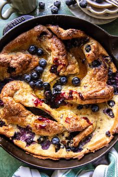 a pan filled with blueberries and chicken on top of a green table cloth next to utensils